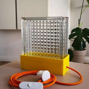 K&ouml;nnte beinhalten: Eine gelbe und klare Glastischlampe mit einem gerippten Glasschirm und einem orangefarbenen Kabel mit einem wei&szlig;en Schalter.