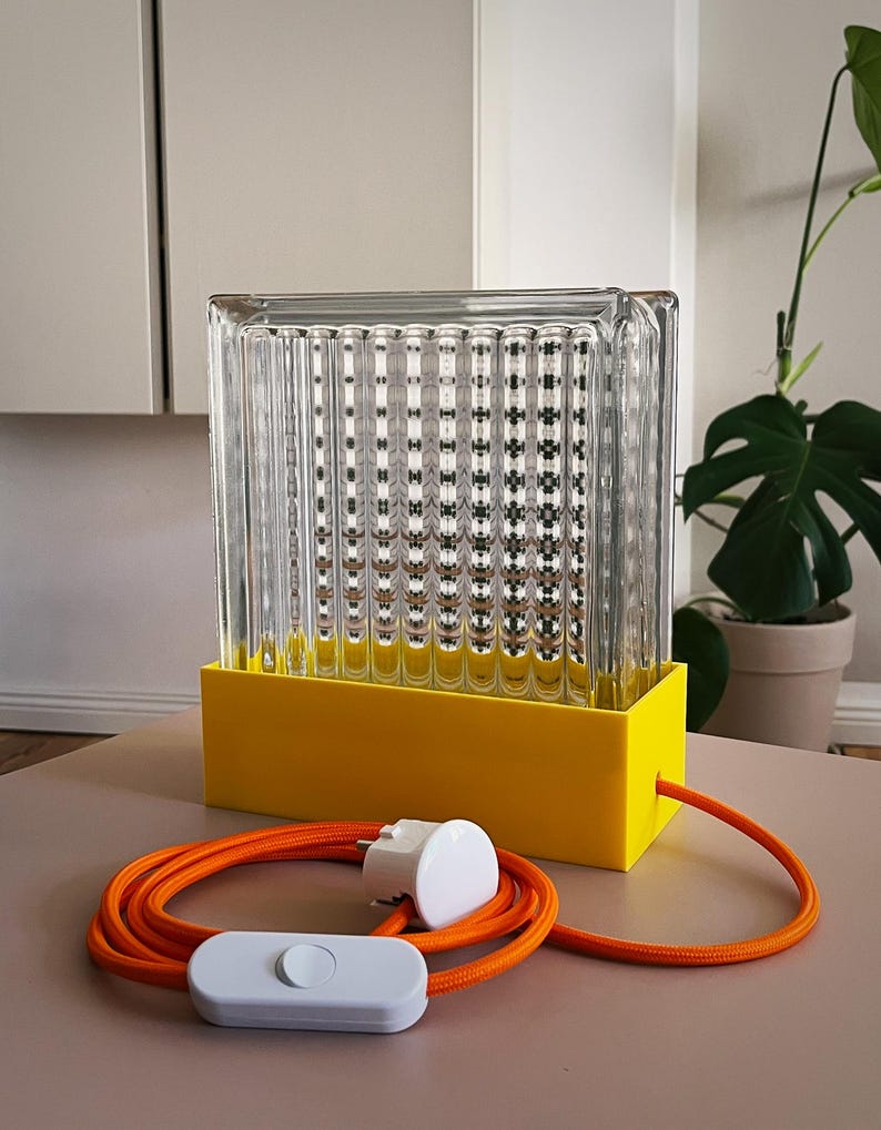K&ouml;nnte beinhalten: Eine gelbe und klare Glastischlampe mit einem gerippten Glasschirm und einem orangefarbenen Kabel mit einem wei&szlig;en Schalter.