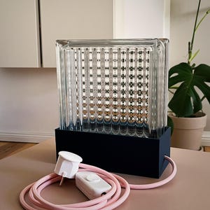 K&ouml;nnte beinhalten: Eine Glaslampe mit schwarzem Sockel und rosa Kabel. Die Lampe hat einen strukturierten Glasschirm und einen wei&szlig;en Schalter am Kabel.