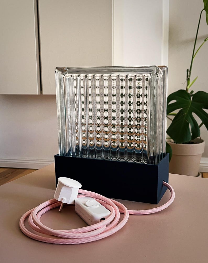 K&ouml;nnte beinhalten: Eine Glaslampe mit schwarzem Sockel und rosa Kabel. Die Lampe hat einen strukturierten Glasschirm und einen wei&szlig;en Schalter am Kabel.