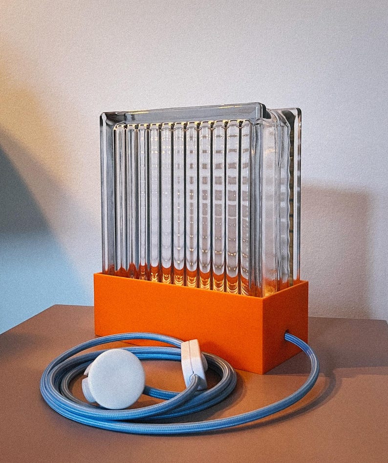 K&ouml;nnte beinhalten: Eine Glaslampe mit gerippter Textur und einem orangefarbenen Sockel. Die Lampe hat ein blaues Kabel mit einem wei&szlig;en Stecker.