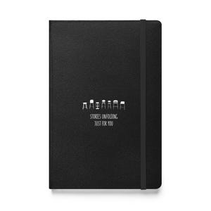Può includere: Quaderno nero con copertina strutturata e chiusura con fascia elastica. Il quaderno presenta una grafica bianca di sedie stilizzate e il testo "STORIES UNFOLDING JUST FOR YOU".