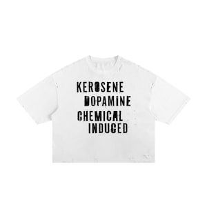 Puede incluir: Una camiseta blanca de manga corta con una textura desgastada y pequeños agujeros a lo largo del cuello y el dobladillo. El centro presenta texto negro en letras de bloque que dice KEROSENE, DOPAMINE, CHEMICAL, INDUCED en estilo apilado.