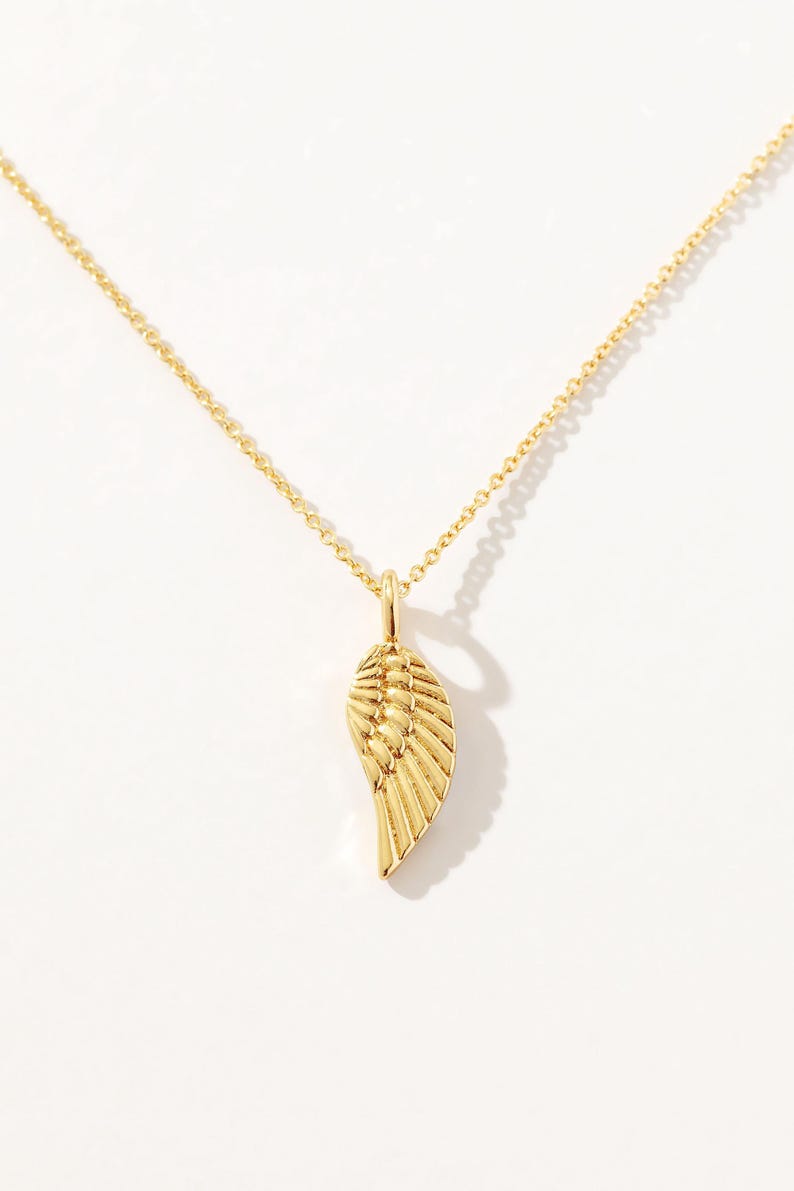 Puede incluir: Un collar de cadena de oro con un delicado colgante de ala de oro.