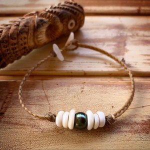 May include: A brown braided cord bracelet with white shell beads and a dark green pearl in the center.