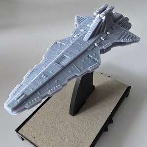 Puede incluir: Un modelo gris detallado de una nave espacial Star Destroyer en un soporte de exhibición negro. El soporte está sobre una base gris texturizada.