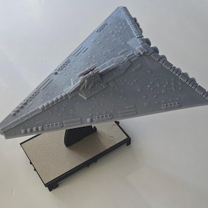 May include: A gray model of a Star Wars spaceship on a gray base. The spaceship has a pointed nose and a flat bottom.