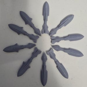 May include: A circular arrangement of grey, spear-like objects with a futuristic design. Each object has a pointed end and intricate surface details, possibly related to technology or science fiction.