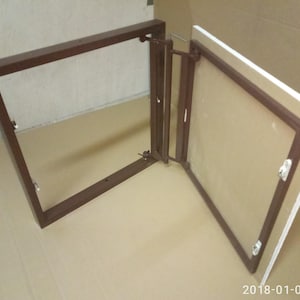 Könnte beinhalten: Ein brauner Metallrahmen mit rechteckiger Öffnung, verbunden mit einer Scharniertafel mit klarer Oberfläche. Die Tafel ist braun umrahmt und hat eine weiße Rückseite. Der Rahmen ist offen, und die Tafel ist teilweise geöffnet.