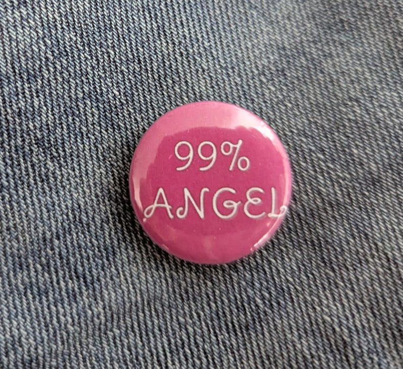 May include: A round, pink button with the text "99% ANGEL" in white script. The button is set against a denim background.