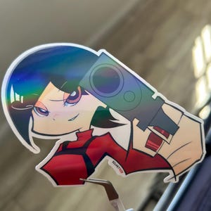 May include: A holographic sticker depicting an anime-style character with a gun. The character has black hair and red clothing. The sticker has a glossy finish and the text "VELVET RED".