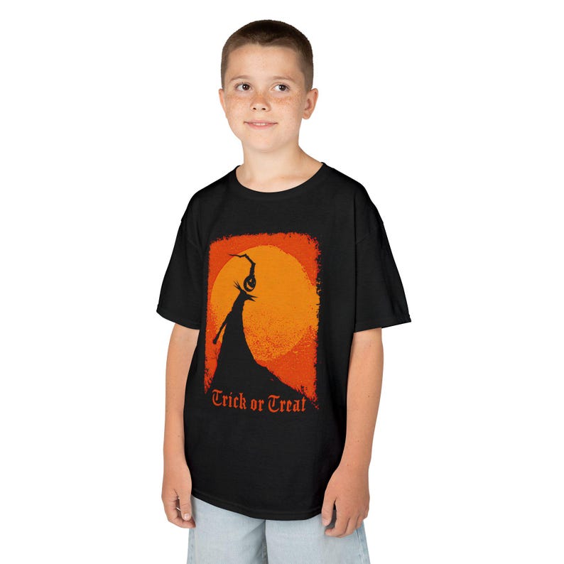 Puede incluir: Camiseta negra con un dise&ntilde;o de Halloween. El gr&aacute;fico muestra la silueta de una figura con una larga capa contra un sol naranja, con las palabras "Trick or Treat" debajo. La camiseta est&aacute; hecha de una tela suave.