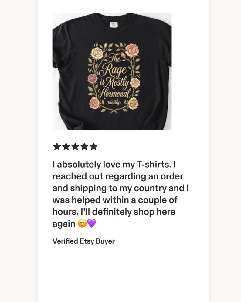 Może przedstawiać: Czarny t-shirt z kr&oacute;tkim rękawem z centralną grafiką wieńca z r&oacute;żowych, ż&oacute;łtych i białych r&oacute;ż. Tekst wewnątrz wieńca brzmi, The Rage is Mostly Hormonal, a słowo mostly powt&oacute;rzono mniejszą czcionką tuż pod gł&oacute;wnym napisem.