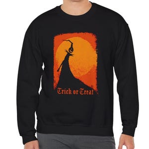 May include: A black long-sleeve sweatshirt featuring a graphic print of a silhouette figure standing on a hill against a large orange moon. Above the figure is a hanging jack-o'-lantern. The text "Trick or Treat" is printed in orange below.