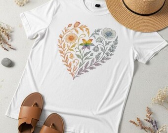 Könnte beinhalten: Weißes T-Shirt mit einem floralen Herzdesign in Regenbogenfarben. Das Herz besteht aus verschiedenen Blumen und Blättern. Ein Strohhut und braune Sandalen sind ebenfalls zu sehen.