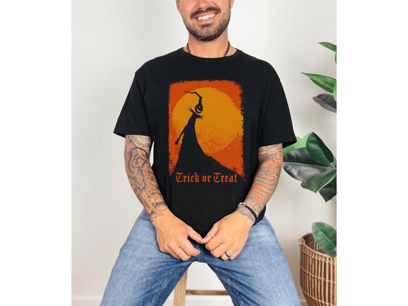 Puede incluir: Camiseta negra con un dise&ntilde;o tem&aacute;tico de Halloween. El dise&ntilde;o presenta la silueta de una figura con cabeza de calabaza contra un sol naranja, con las palabras "Trick or Treat" en naranja.