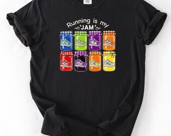 Könnte beinhalten: Schwarzes T-Shirt mit dem Schriftzug "Running is my JAM" über einer Grafik von acht bunten Marmeladengläsern, die jeweils einen andersfarbigen Laufschuh enthalten. Die Gläser haben verschiedene Deckelfarben und Schuhdesigns.