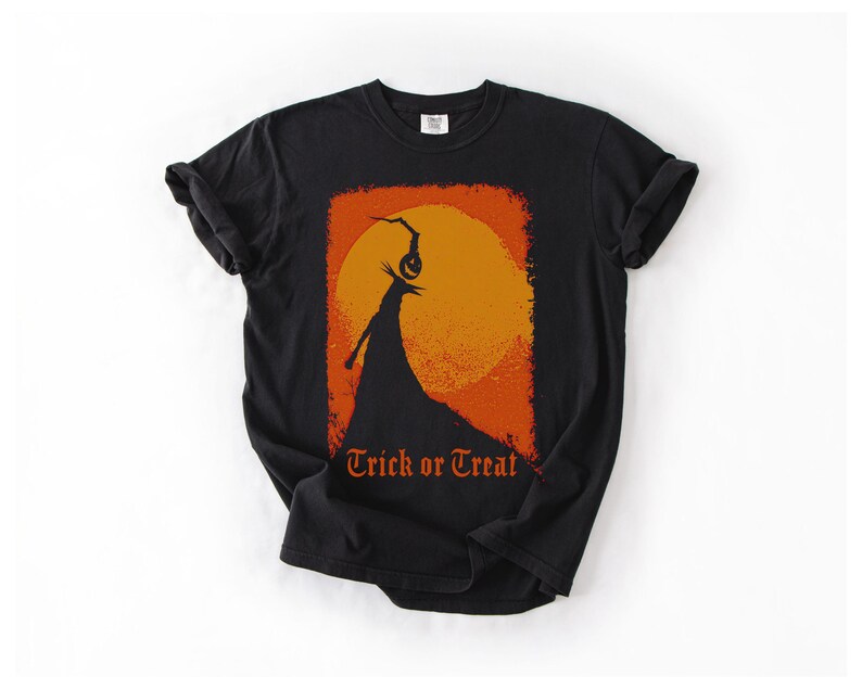 Puede incluir: Camiseta negra con un dise&ntilde;o de Halloween. El gr&aacute;fico incluye una figura silueteada con una cabeza de calabaza contra un sol naranja, con las palabras "Trick or Treat" en escritura naranja.