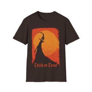 Puede incluir: Camiseta marr&oacute;n con un dise&ntilde;o de Halloween. El gr&aacute;fico muestra una silueta con una cabeza de calabaza frente a un sol naranja, con las palabras "Trick or Treat" debajo.