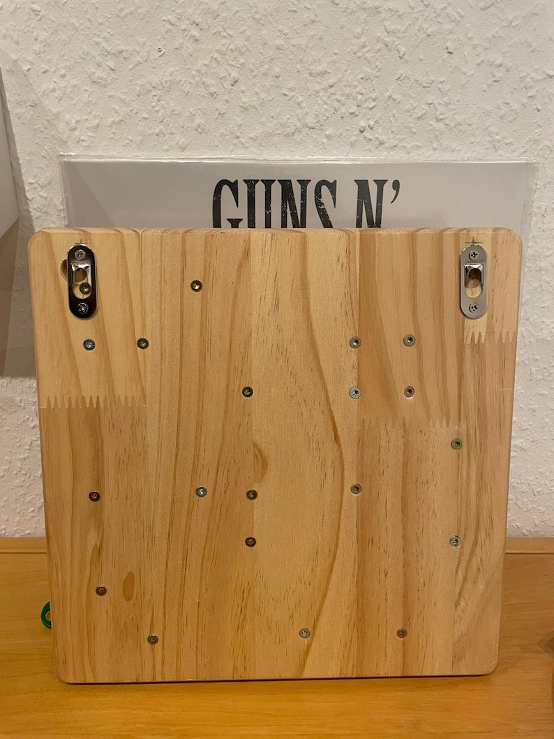 May include: A wooden backboard with multiple screws and two metal hooks. The backboard is light brown and has a natural wood grain.