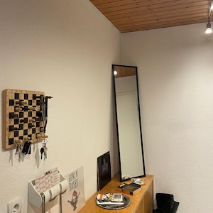 May include: A wooden entryway with a white wall, a wooden ceiling, a black mirror, a wooden shelf with a Guns N' Roses album, a white key holder, and a chessboard with chess pieces.