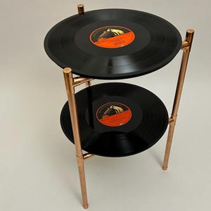 Op de afbeelding: Een tweelaagse bijzettafel gemaakt van koperen buizen en vintage vinylplaten. De tafel heeft een eenvoudig, industrieel ontwerp en zou een geweldige aanvulling zijn op elk modern huis.