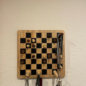 May include: A wooden magnetic chessboard with white and black squares, with chess pieces on the board. The board is mounted on a wall and has key hooks on the bottom. There are keys and a pocket knife hanging on the hooks.