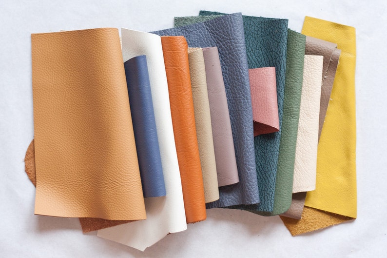 May include: A collection of leather swatches in various colors, including tan, blue, orange, white, and green. The swatches have a textured surface and are arranged in a fan shape, showcasing the different colors and textures available.