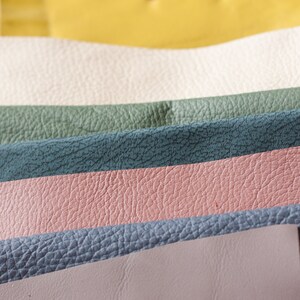 May include: Close-up of various colorful leather swatches. The swatches are arranged in horizontal rows, showcasing a range of colors including yellow, orange, cream, green, teal, pink, blue, and lavender. The leather has a textured grain.