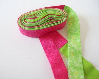 May include: A roll of pink and green fabric with a white background. The fabric is folded in half and tied in a knot.
