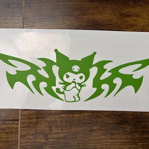 May include: A bright green vinyl decal featuring a stylized cartoon character with pointed ears and a skull emblem on its forehead, flanked by sharp, symmetrical tribal-inspired wing patterns on a white adhesive backing sheet.
