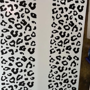 May include: A sheet of white material with a repeating black leopard print pattern. The pattern consists of irregular black spots and shapes, creating a bold and eye-catching design. The sheet is likely used for crafts or decorative purposes.