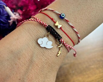 Könnte beinhalten: Drei rote und weiße Armbänder aus Kordel mit Anhängern. Die Anhänger sind ein blaues böses Auge, ein goldener Schmetterling, eine goldene Wolke und ein goldener Sternschnuppen.