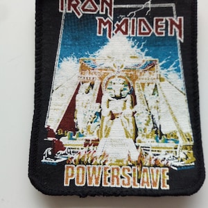 Op de afbeelding: Zwarte Iron Maiden Powerslave patch met een kleurrijk beeld van een farao voor een piramide. De patch heeft een zwarte rand met witte stiksels.