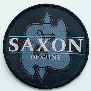 Op de afbeelding: Een ronde zwarte en grijze patch met een gestileerd logo en de tekst "SAXON DESTINY".