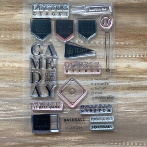 May include: Clear stamp set with baseball-themed designs. Includes text like "Little League," "Game Day," and "Baseball." Features baseballs, bats, and diamond shapes. Perfect for scrapbooking or crafting.