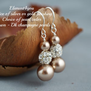 May include: A pair of dangle earrings with champagne colored pearls and clear crystal beads. The earrings are silver or gold tone and have a choice of pearl color.