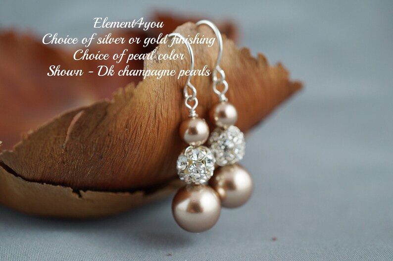 May include: A pair of dangle earrings with champagne colored pearls and clear crystal beads. The earrings are silver or gold tone and have a choice of pearl color.