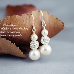 May include: A pair of dangle earrings with ivory pearls and crystal accents. The earrings are available in silver or gold finishes. "Element 4 you" is written on the brown background.