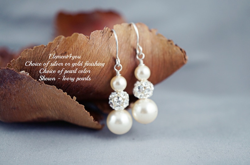May include: A pair of dangle earrings with ivory pearls and crystal accents. The earrings are available in silver or gold finishes. "Element 4 you" is written on the brown background.