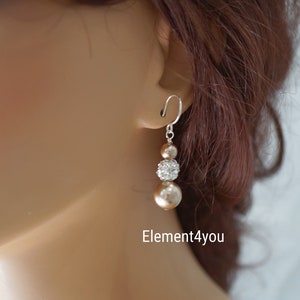 May include: A pair of dangle earrings with three beads. The top bead is a sparkly clear rhinestone, the middle bead is a champagne colored pearl, and the bottom bead is a larger champagne colored pearl. The earrings are silver.