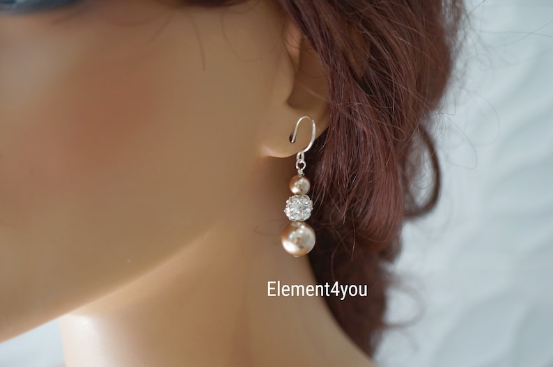 May include: A pair of dangle earrings with three beads. The top bead is a sparkly clear rhinestone, the middle bead is a champagne colored pearl, and the bottom bead is a larger champagne colored pearl. The earrings are silver.