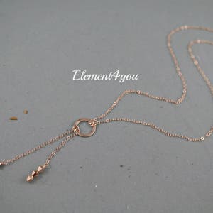 May include: A rose gold necklace with a circle pendant and two dangling strands of beads. The necklace is on a gray background.