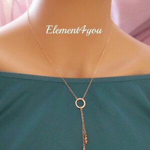 May include: A rose gold necklace with a circle pendant and a dangling chain with small gold beads. The necklace is on a mannequin wearing a teal shirt. The text "Element4you" is visible on the shirt.