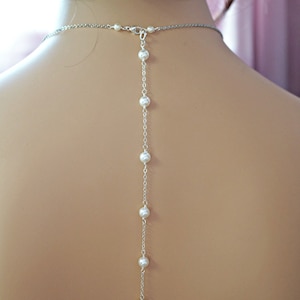May include: A silver chain necklace with white pearl beads. The necklace is long and hangs down the back of the neck. The necklace is called "Element4you".