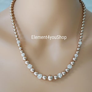 May include: A gold necklace with small, round, pearl-like beads and clear rhinestone accents. The necklace is on a mannequin's neck.