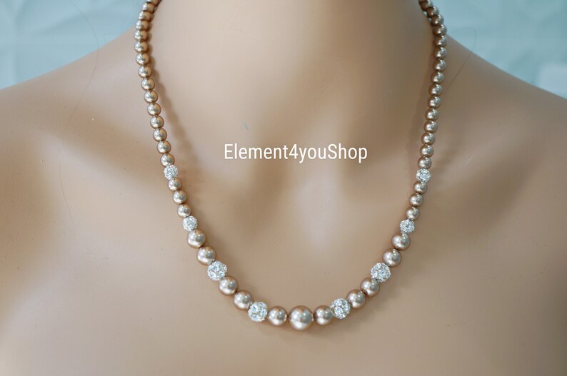 May include: A gold necklace with small, round, pearl-like beads and clear rhinestone accents. The necklace is on a mannequin's neck.