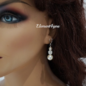 May include: Silver dangle earrings with a pearl and crystal design. The earrings feature three pearls and a crystal cluster.