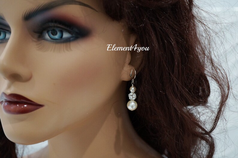 May include: Silver dangle earrings with a pearl and crystal design. The earrings feature three pearls and a crystal cluster.
