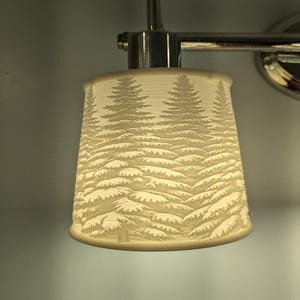 May include: A white light fixture with a frosted glass shade featuring a silhouette of a snowy forest scene.